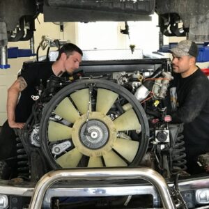 two auto repair men working on a big engine